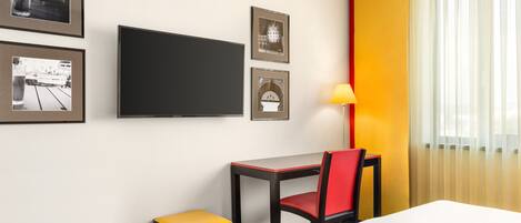 Una habitación de hotel con una cama, un escritorio con una silla, un televisor y cuadros en la pared.