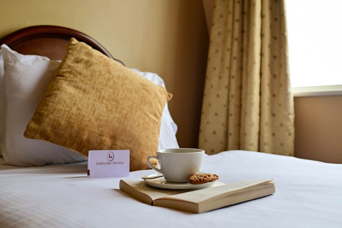 A neatly made bed with a pillow, a cup of coffee, a cookie, and a sign indicating the hotel name.