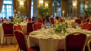Comedor formal con mesas dispuestas para una comida, sillas tapizadas en rojo y un ambiente iluminado por velas.