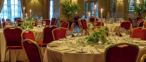 A formal dining room with tables set for a meal, red upholstered chairs, and candlelit ambiance.