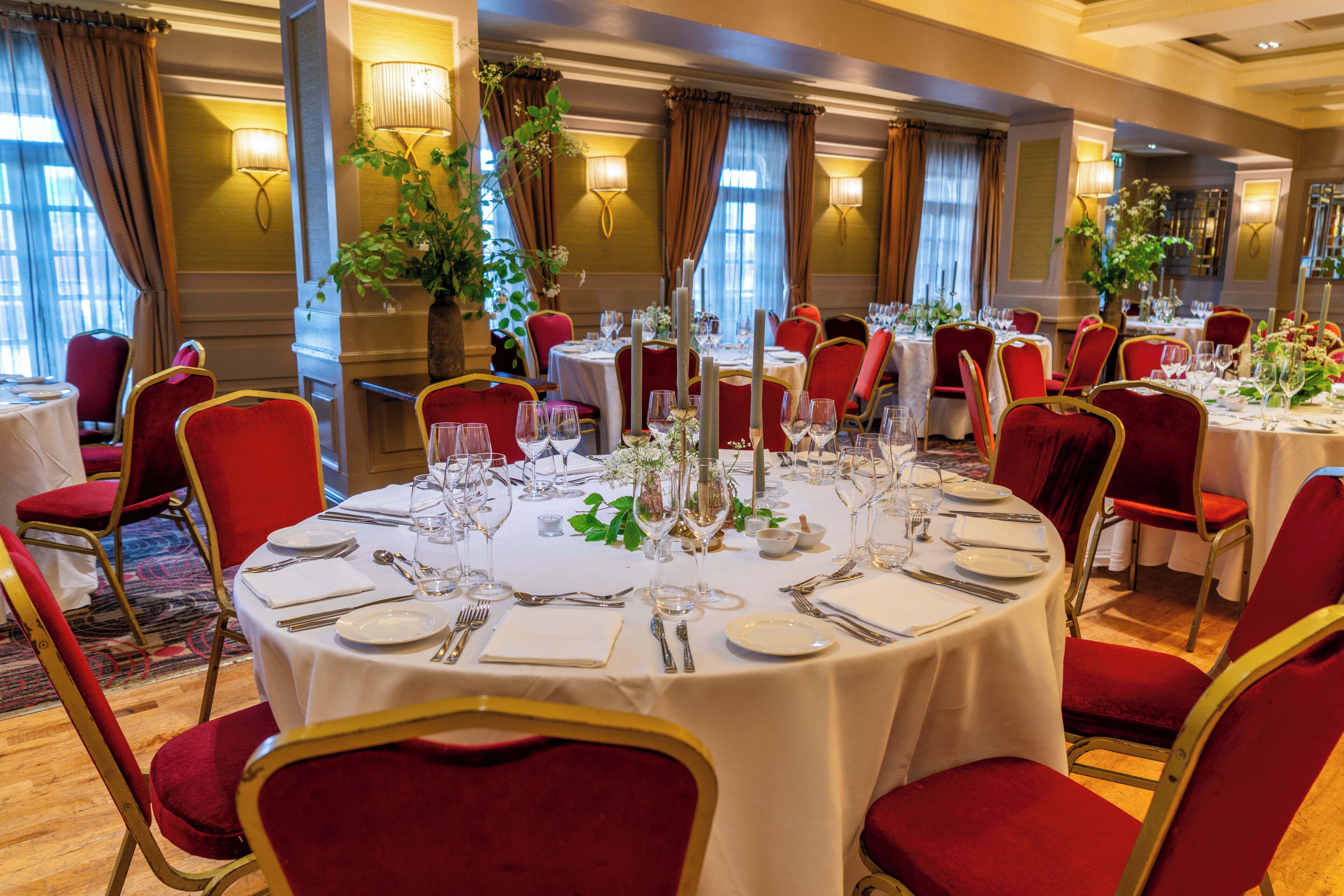 A dining area with round tables, red upholstered chairs, and white tablecloths.