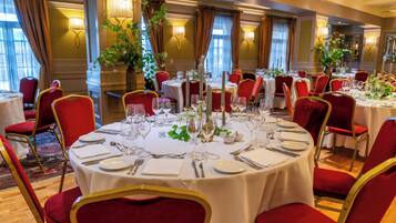 A dining area with round tables, red upholstered chairs, and white tablecloths.