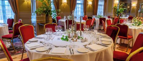 A dining area with round tables, red upholstered chairs, and white tablecloths.