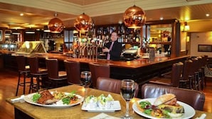 Un restaurante con zona de bar, varias mesas con sillas y un camarero.