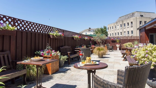Un patio al aire libre con mobiliario de madera, plantas en macetas y cielo despejado.