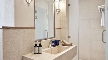 Une salle de bain avec un lavabo en marbre, deux bouteilles de shampoing, un verre bleu et un panier en osier.