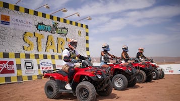 Four riders on quad bikes lined up in front of a sponsorship wall.