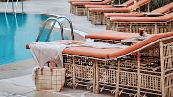 A poolside area with lounge chairs and umbrellas, a pool, and a building with arched windows.