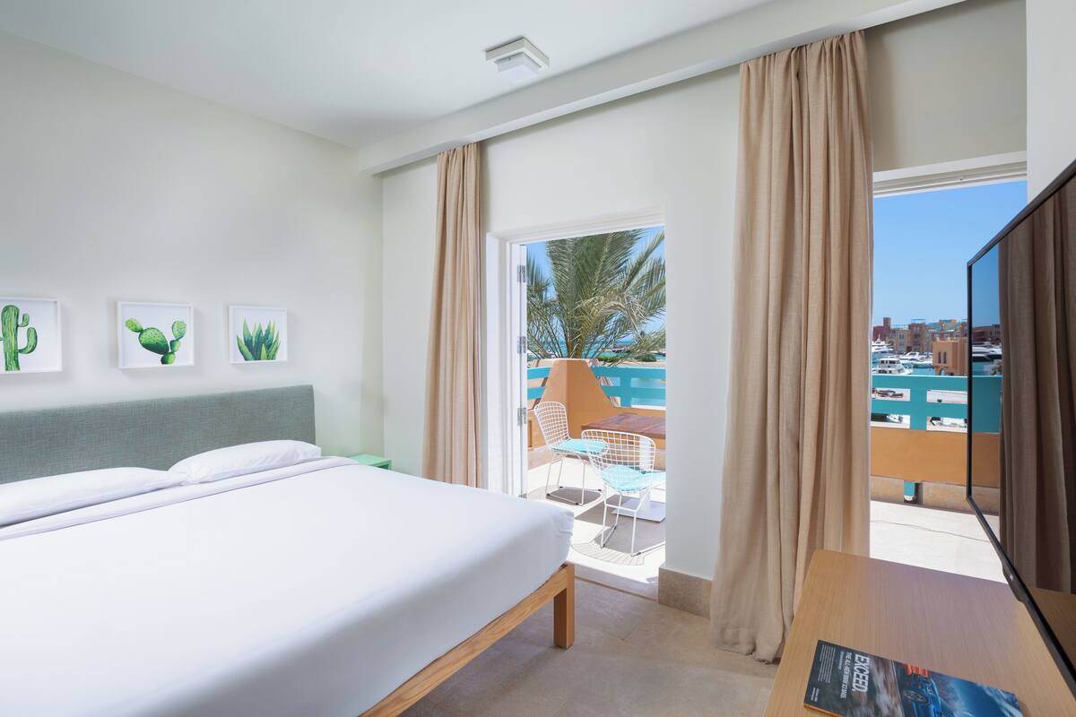 A hotel room with a bed, a TV, and a balcony with a view of the city.