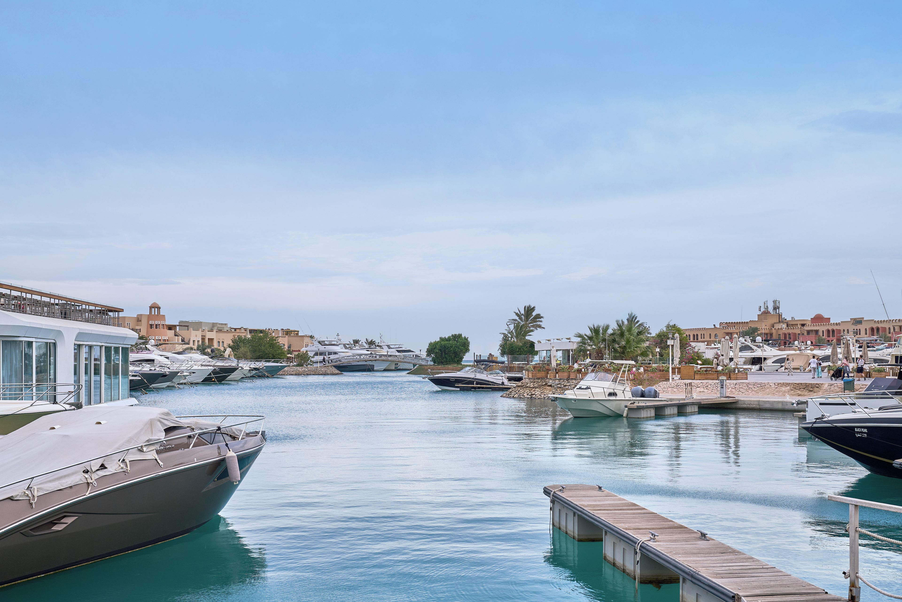 A marina with boats docked, a wooden dock, and buildings in the background.