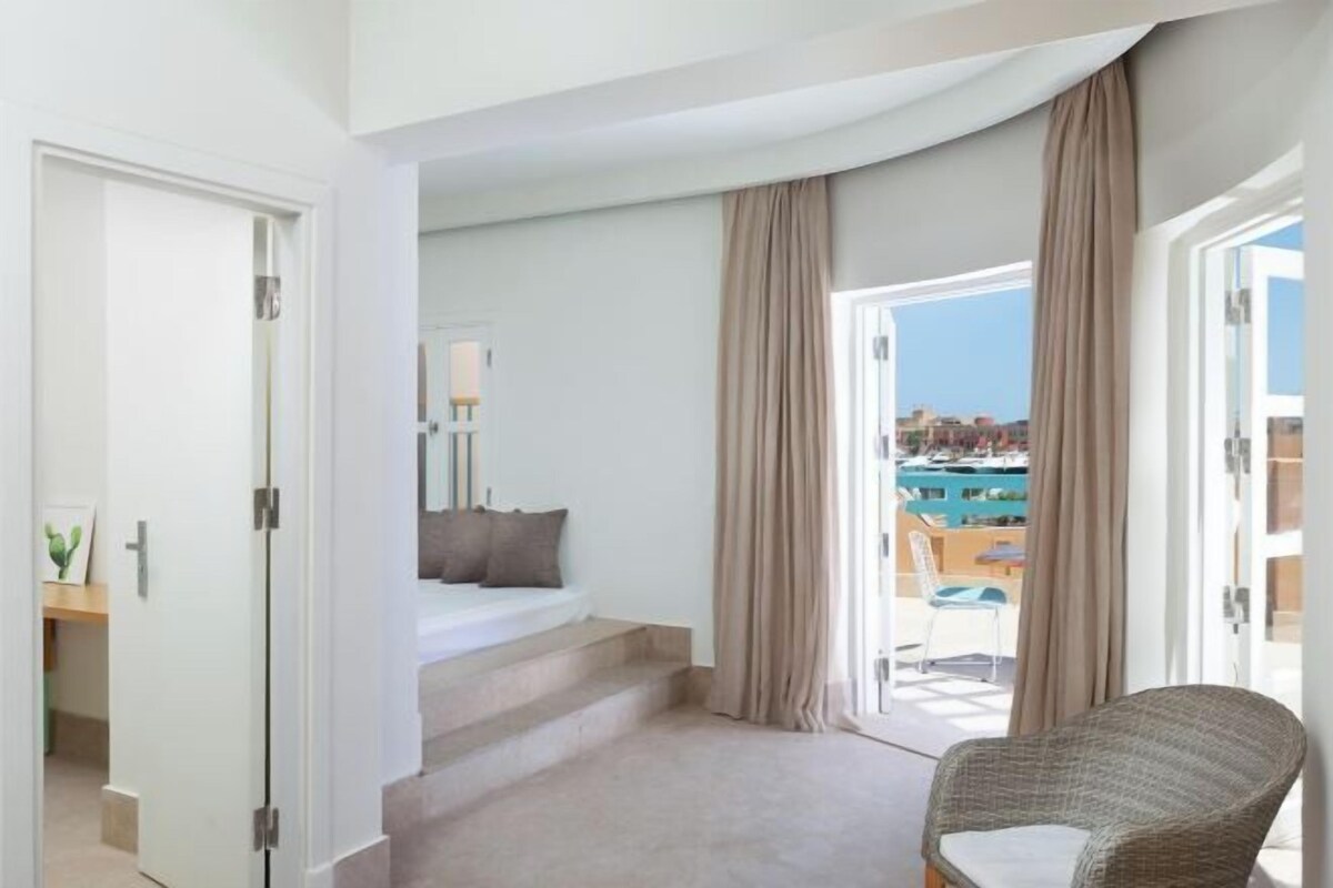 A hotel room with a balcony, a bed, a chair, and a view of the city.