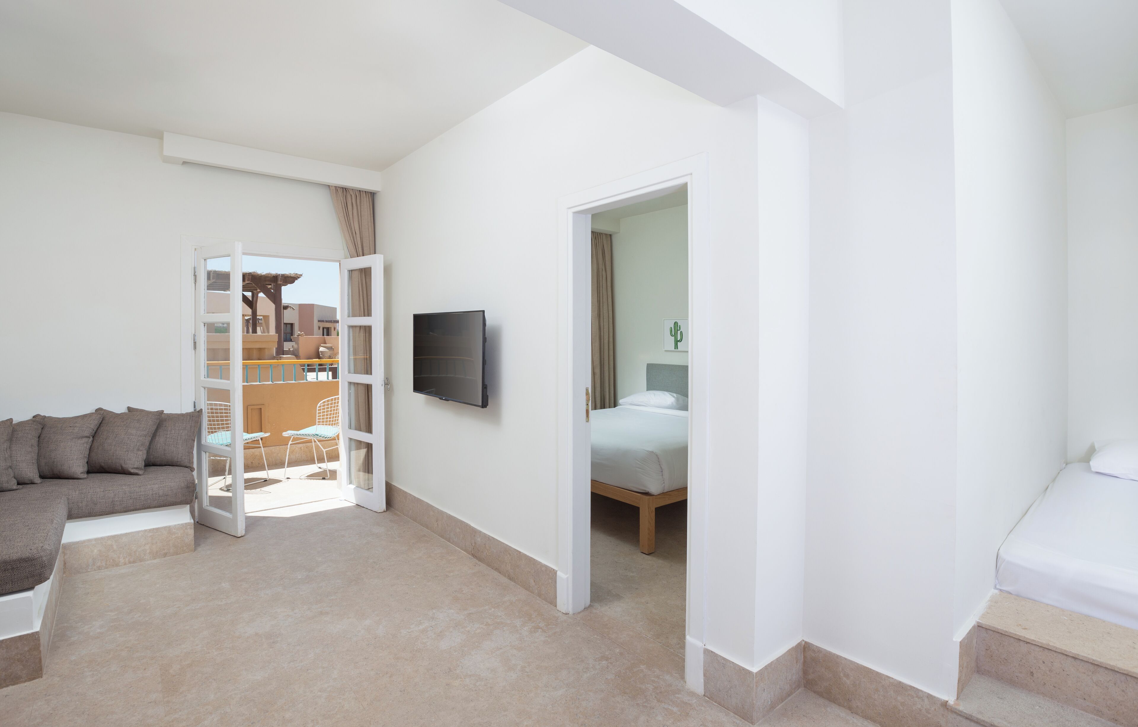 Ein modernes Hotelzimmer mit einer Couch, einem Bett, einem Fernseher und einem Balkon mit Blick auf das Gebäude.