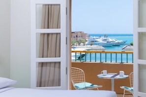 A hotel room with a balcony overlooking a marina with boats and a clear blue sea.