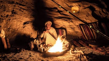 Uma pessoa sentada perto de uma fogueira em um ambiente semelhante a uma caverna, com decoração rústica.