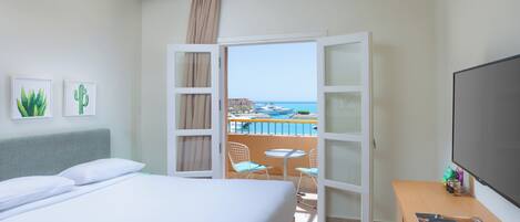 A hotel room with a bed, a desk, a TV, and a balcony with a pool view.