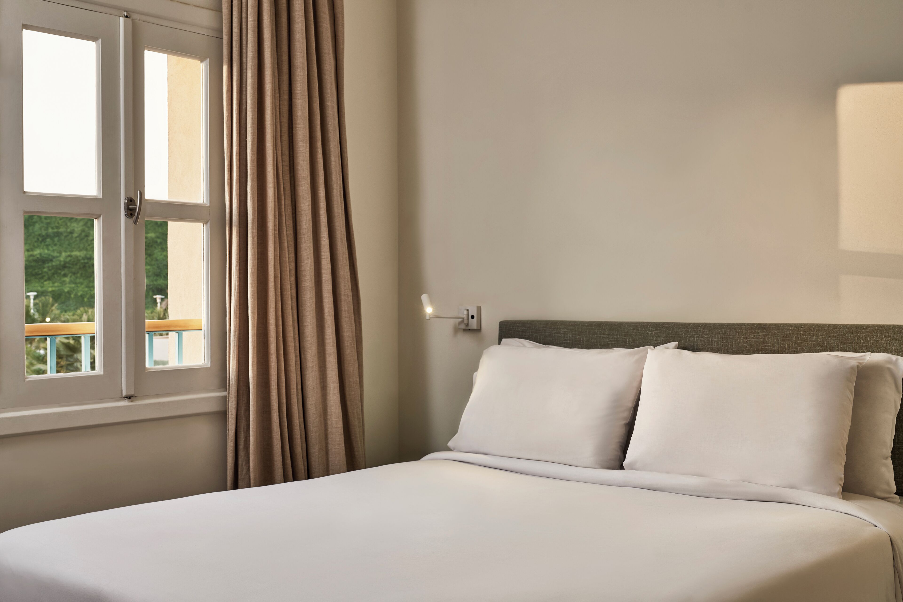 Ein Schlafzimmer mit Bett, Fenster und Blick auf Grün.
