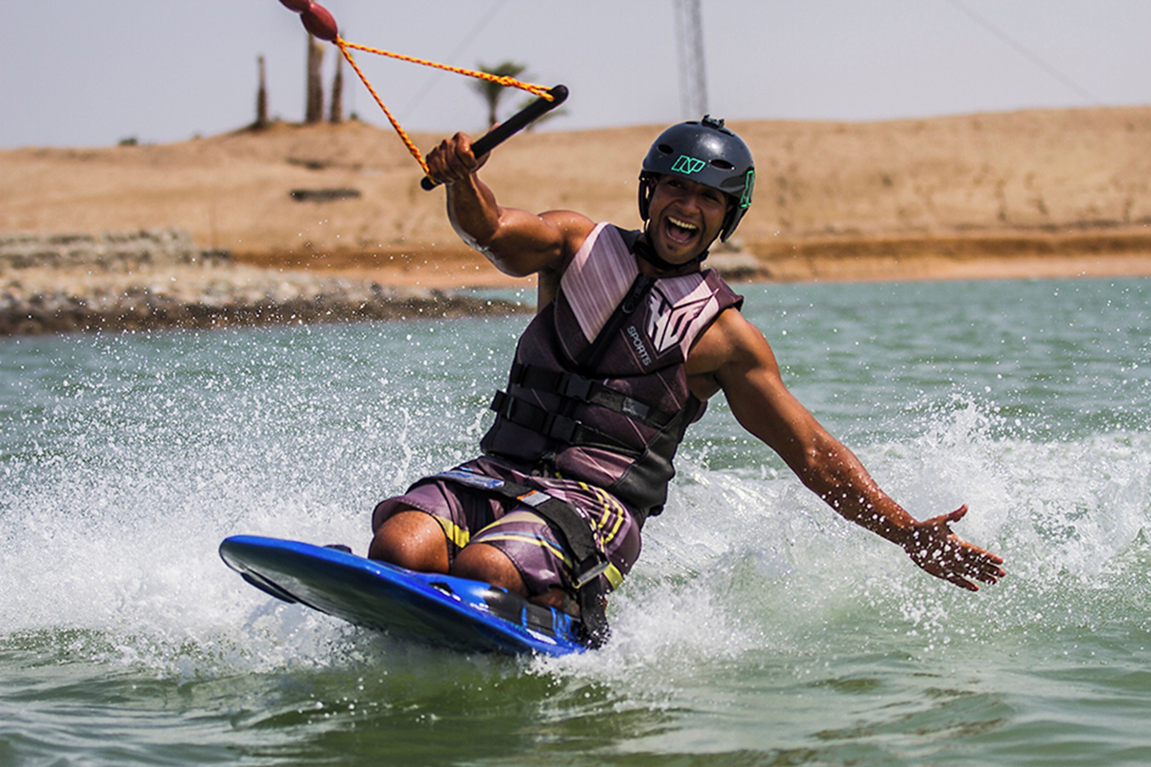 A person water skiing on a blue board, wearing a life vest and helmet.