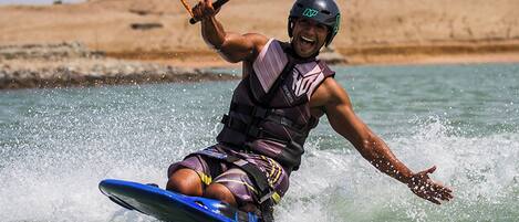 A person water skiing on a blue board, wearing a life vest and helmet.