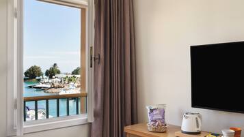 A room with a view of a marina, a wooden desk with a kettle, a bag of snacks, and a cup.