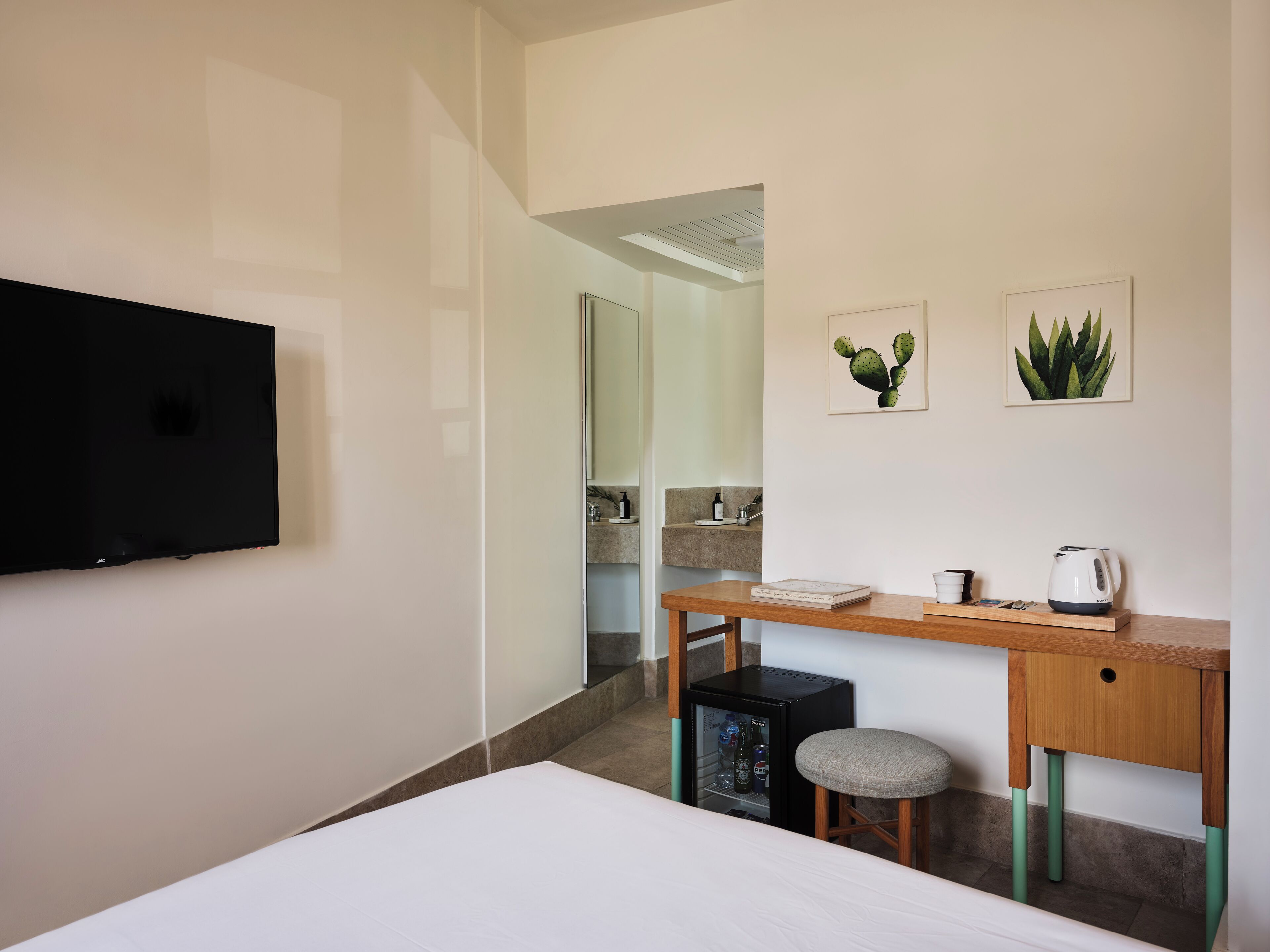 A modern hotel room with a bed, a desk with a chair, a television, and a minibar.