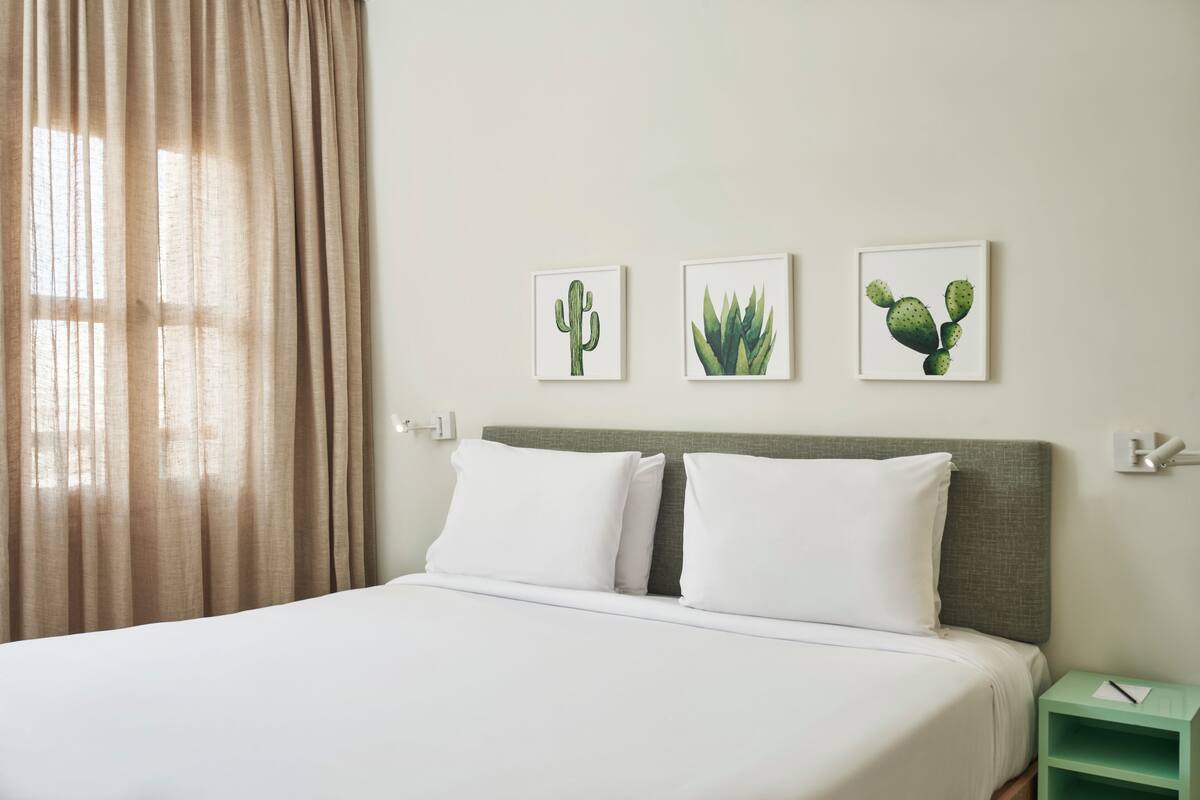 A hotel room with a bed, beige curtains, and three framed cactus pictures on the wall.