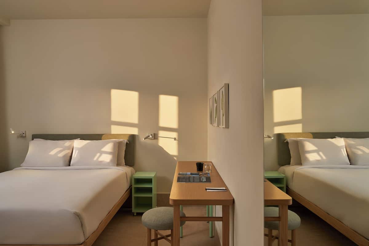 A hotel room with two beds, a desk, and a chair.