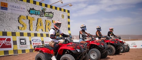 Four riders on quad bikes lined up in front of a sponsorship wall.