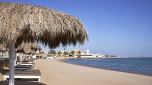 Ein Strand mit Liegestühlen und einem Reetdachschirm.