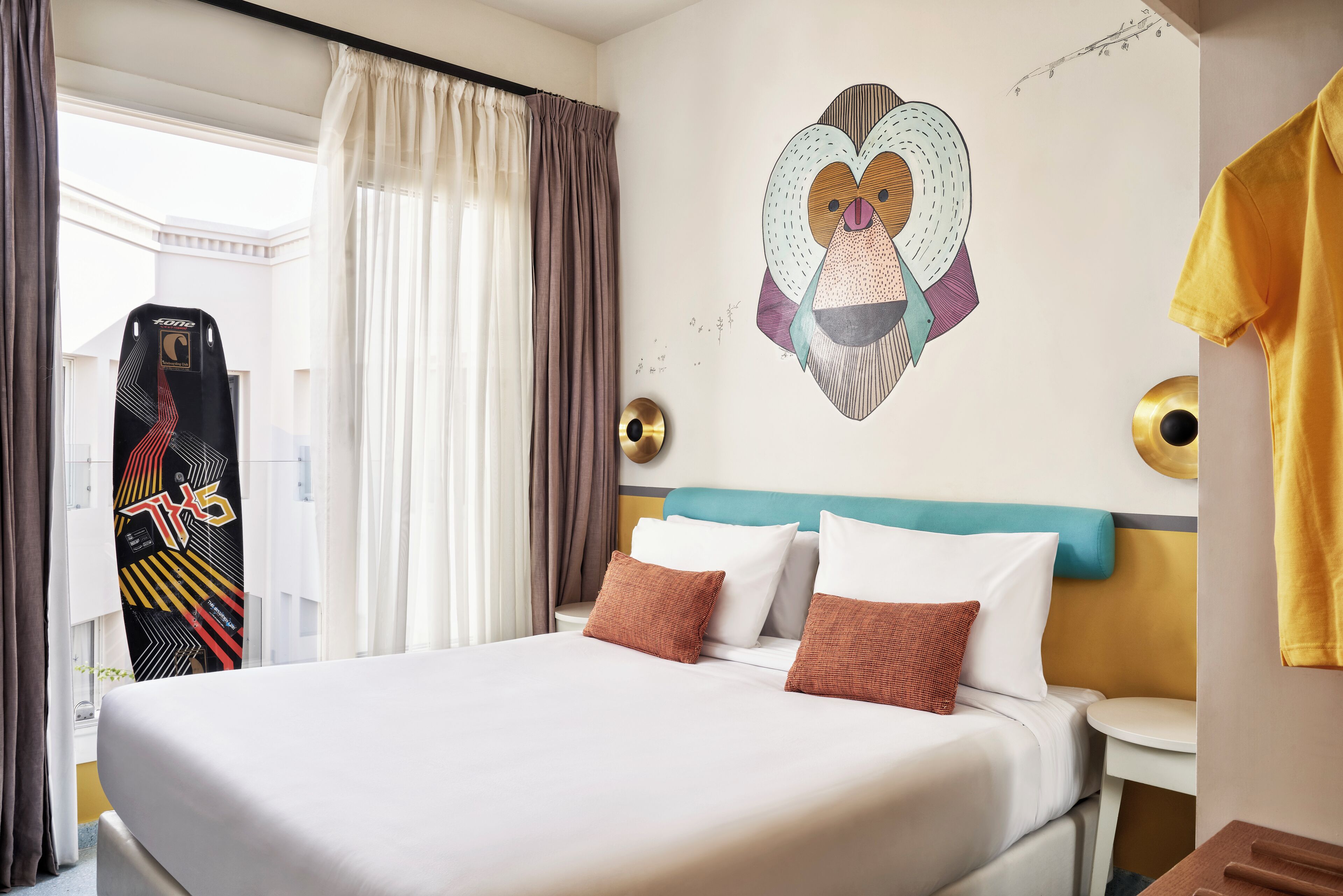 A hotel room with a bed, a wall art of a heart, and a window with curtains.