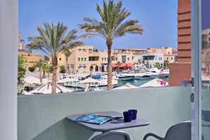 A balcony with a table, two blue cups, and a magazine. In the background, there are palm trees, a marina with boats, and buildings.
