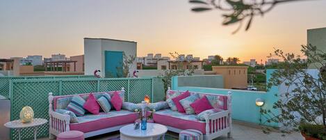 A rooftop terrace with a white sofa set, a round table, and a colorful rug.