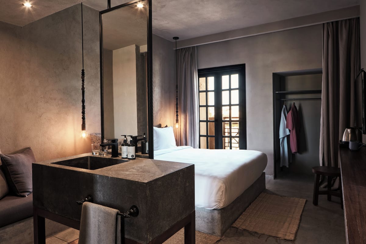 Une chambre d’hôtel moderne dotée d’un grand lit, d’un bureau intégré avec un miroir, d’un petit coin salon et d’une armoire.