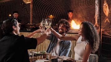 A group of people toasting with wine glasses at a wooden table with a fire in the background.