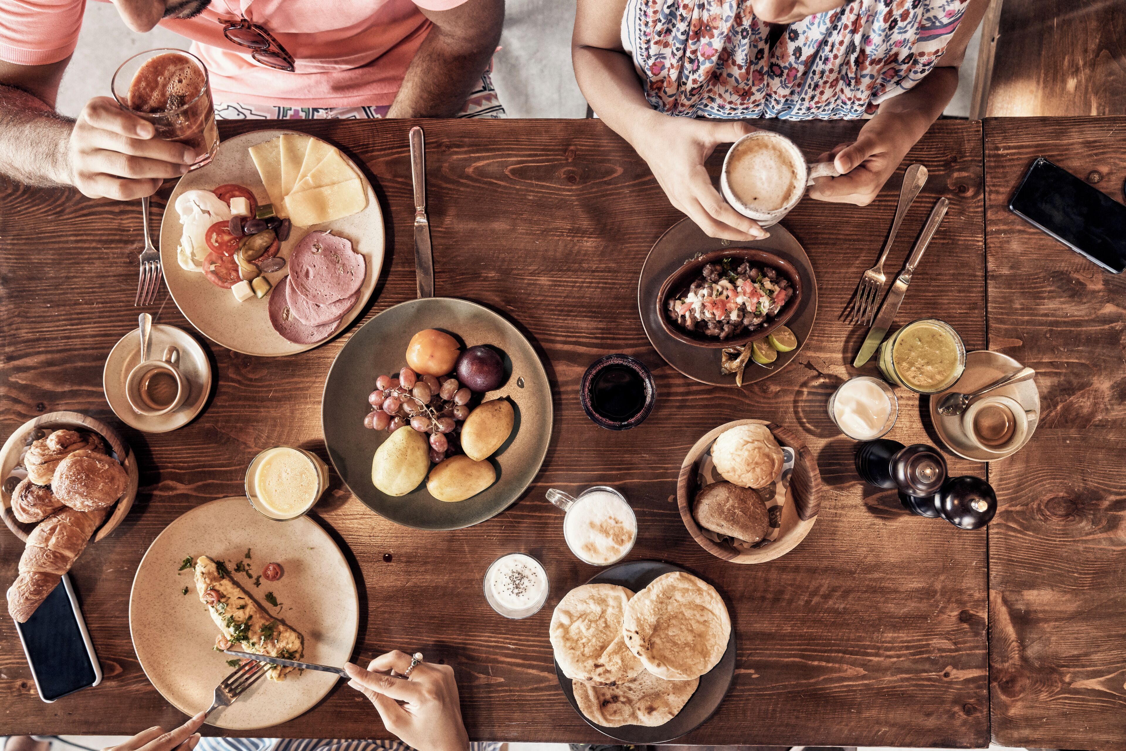 A wooden table with various food items and drinks, including bread, cheese, and a plate of grapes.