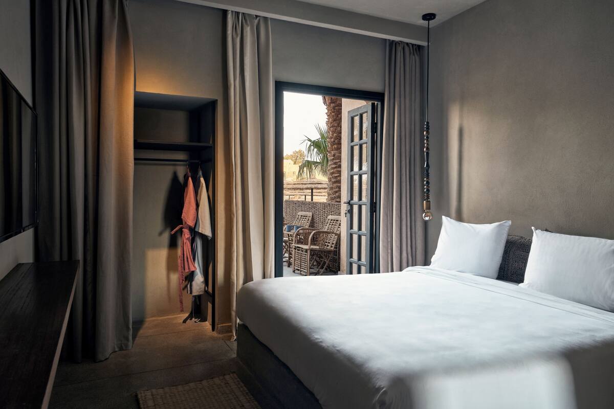 Une chambre d’hôtel avec un grand lit, une armoire et une vue sur un espace extérieur aménagé avec des sièges.