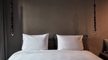 A neatly made bed with white linens and two pillows, a dark headboard, and a hanging light fixture.