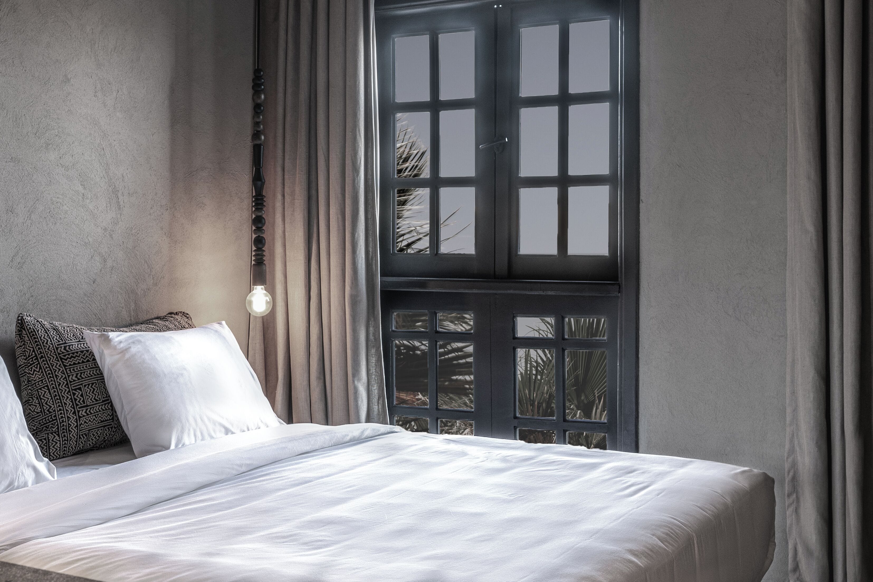 Un dormitorio con una cama grande, una ventana con vistas y una lámpara fijada a la pared.