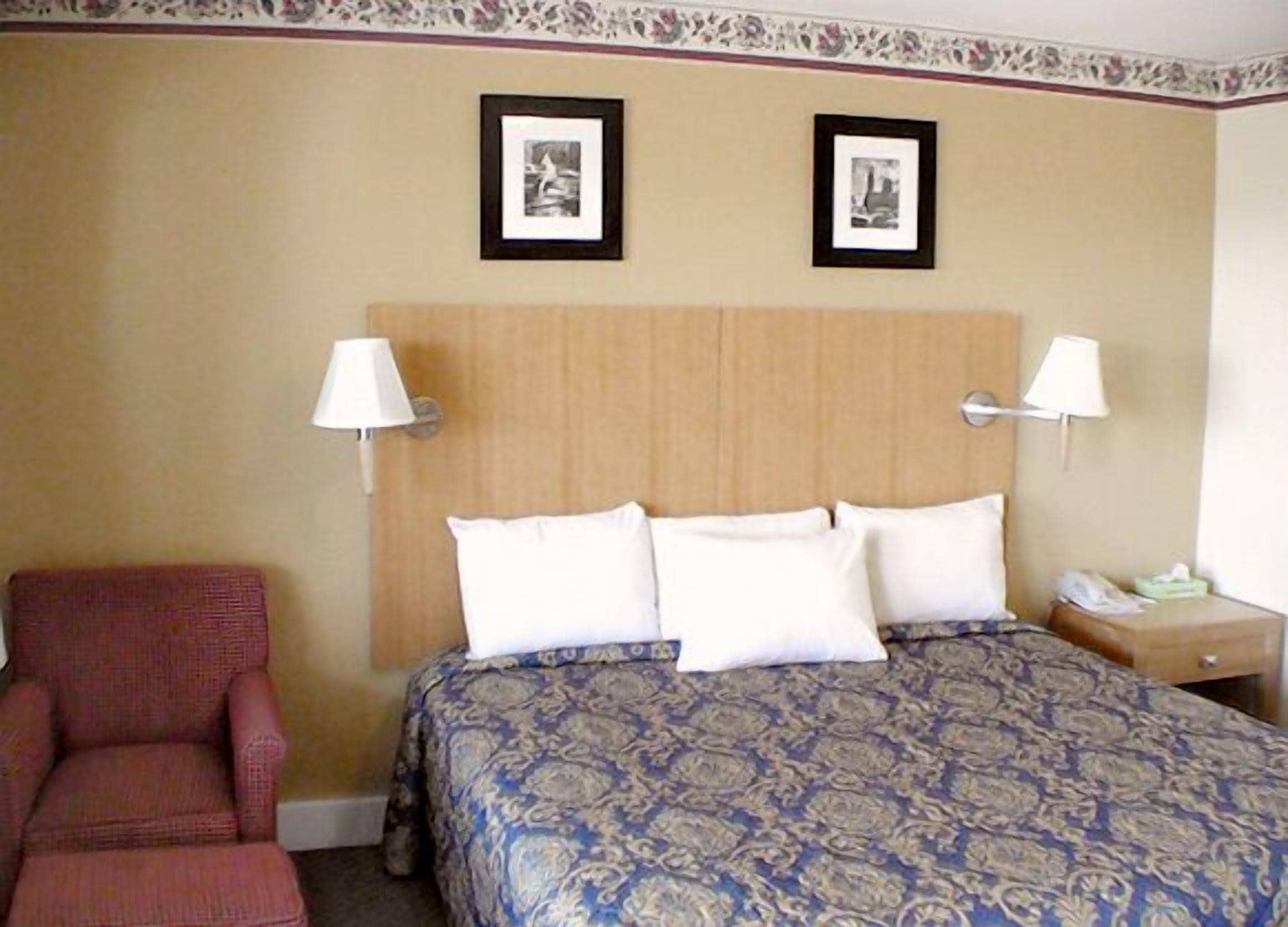 Una camera d'hotel con un letto, due lampade a parete, una sedia e due quadri appesi al muro.