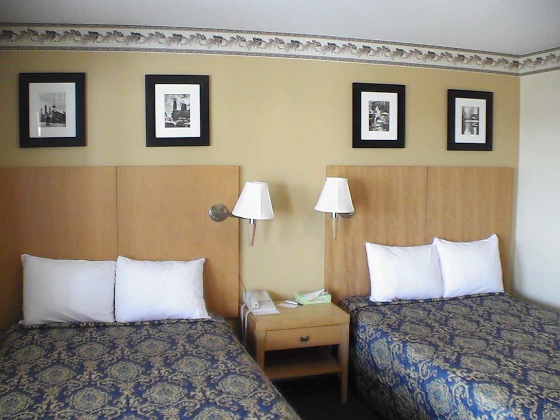 A hotel room with two beds, each with patterned bedding, a wooden headboard, a nightstand with a lamp, and framed pictures on the wall.