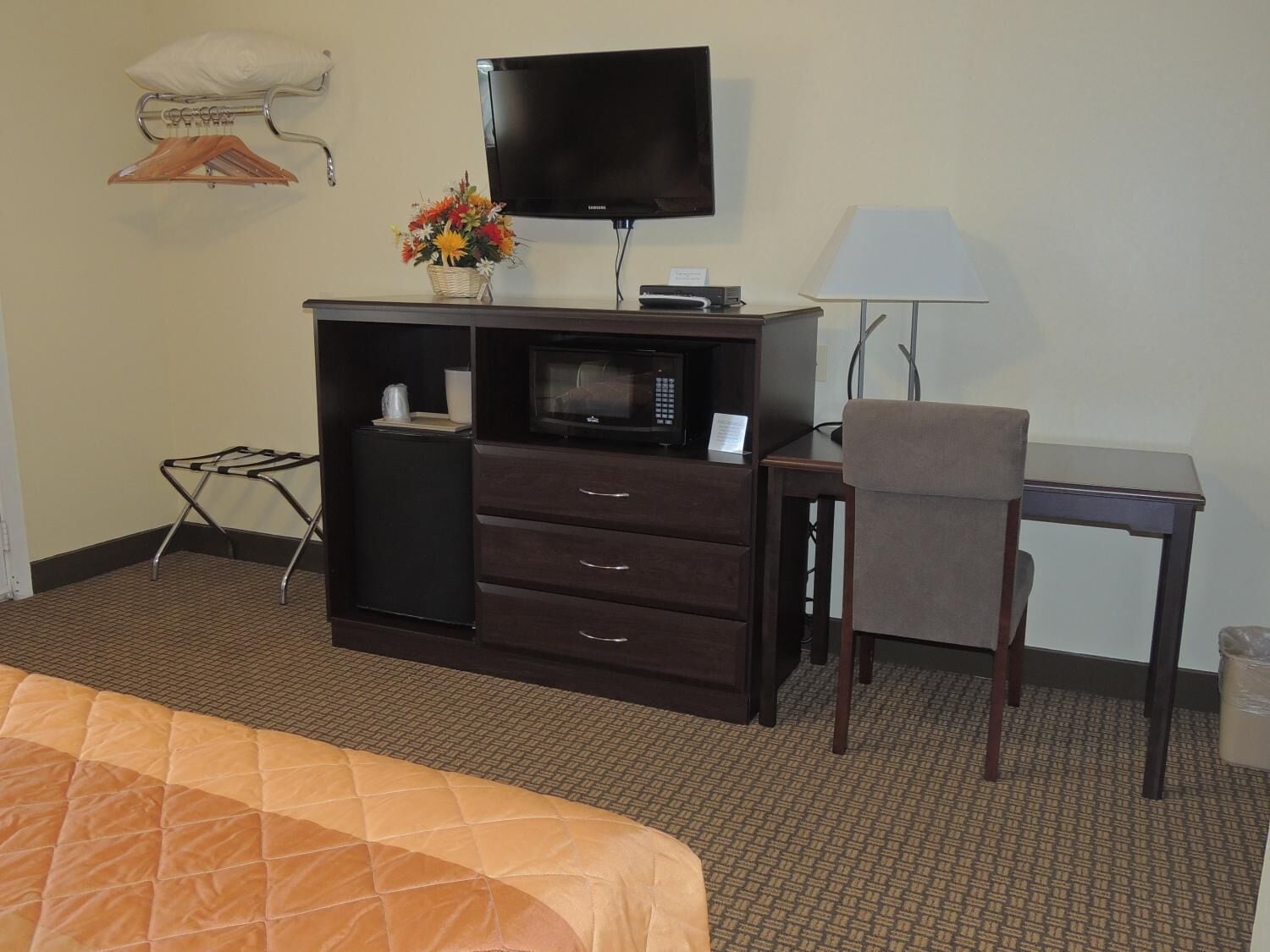 A hotel room with a bed, a desk with a chair, a television, a microwave, a lamp, and a small table.
