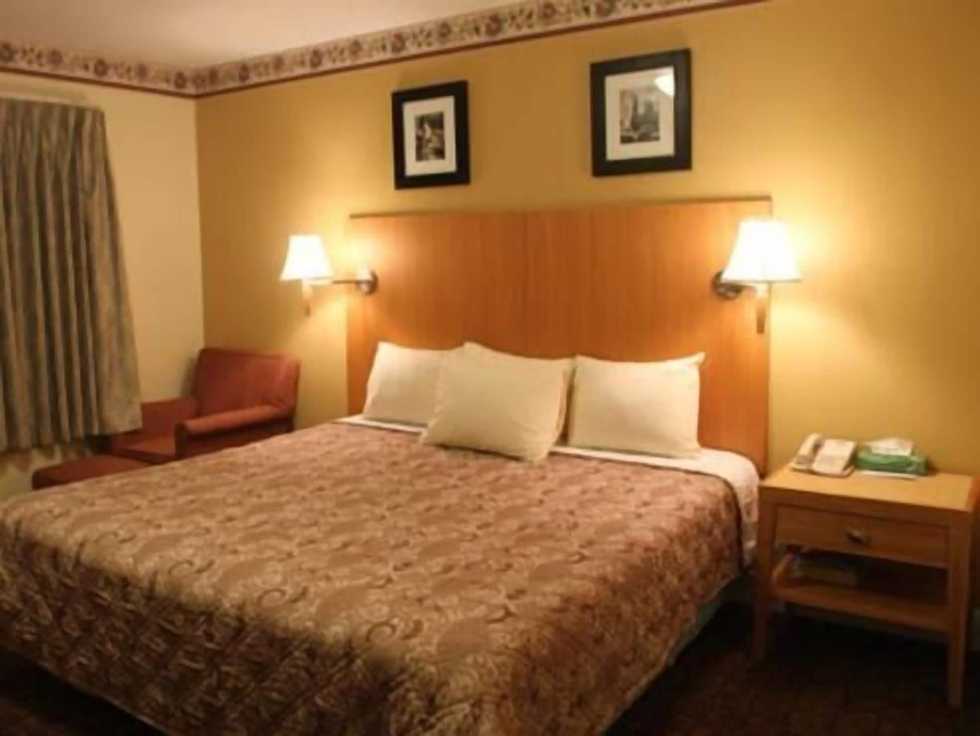 A hotel room with a large bed, two wall-mounted lamps, a chair, and a nightstand with a phone.