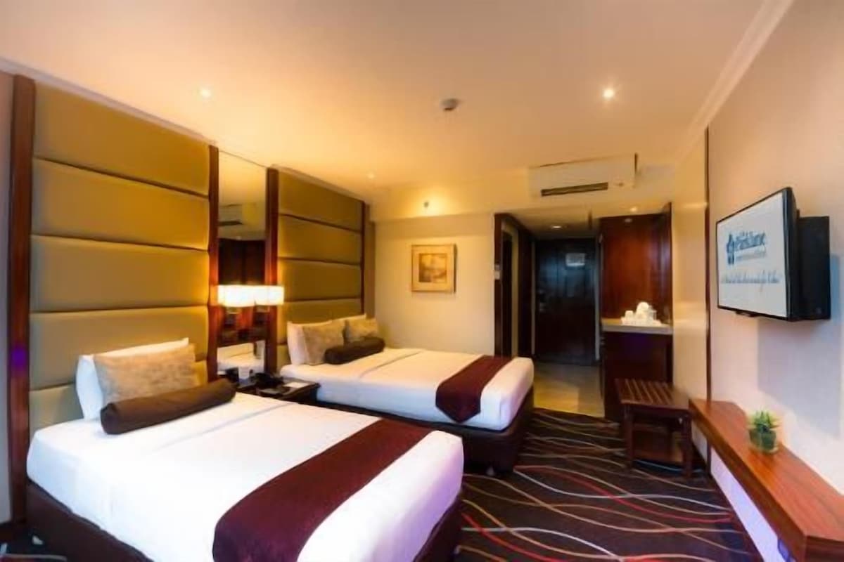 Une chambre d’hôtel avec deux lits, un grand miroir, un téléviseur à écran plat et une petite table agrémentée d’une plante.