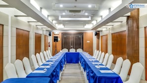 Ein Konferenzraum mit einem langen Tisch, weißen Stühlen und blauen Tischdecken.