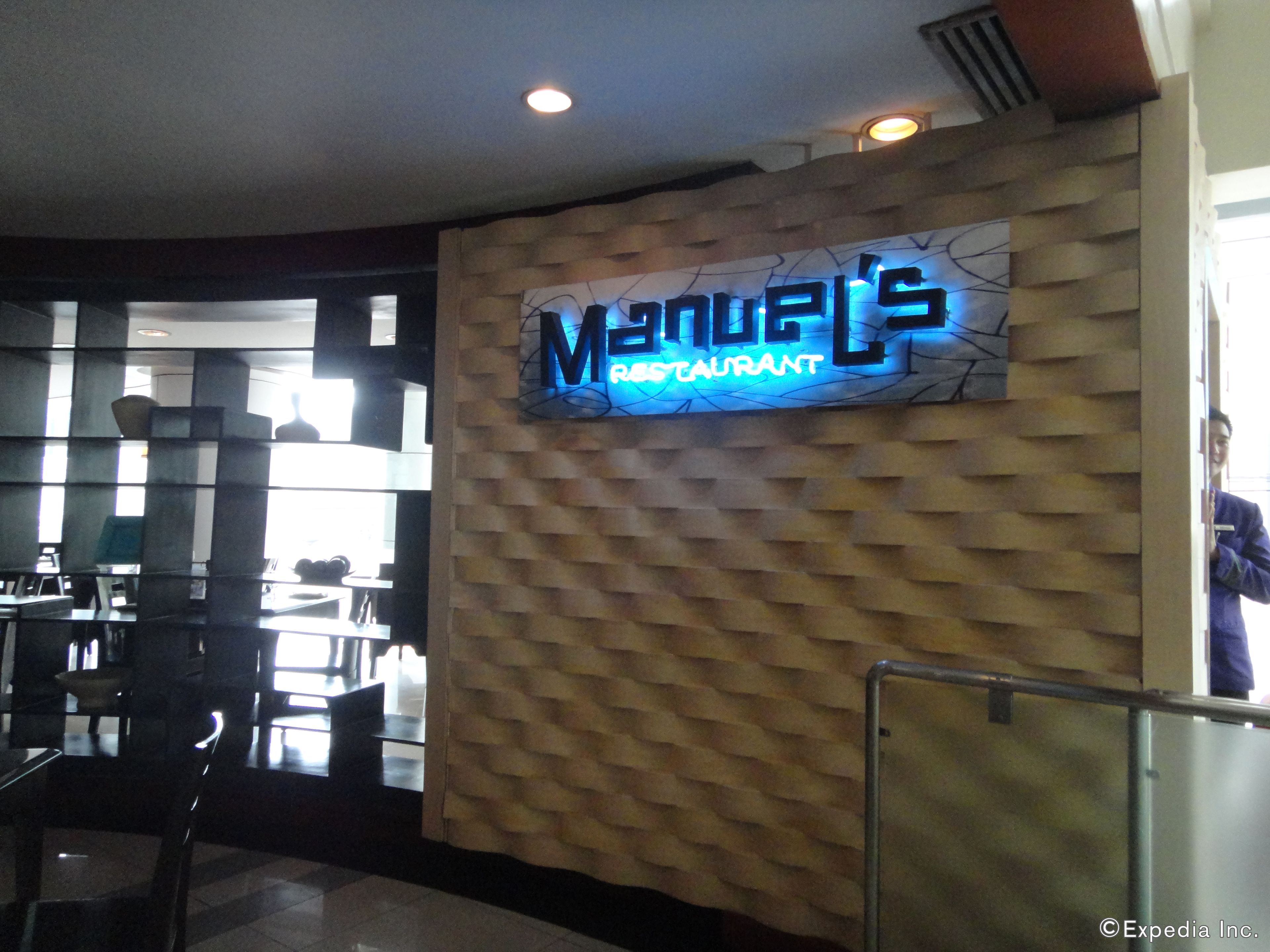 A restaurant interior with a neon sign reading "Manuel's Restaurant" on a textured wall.