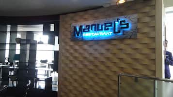 A restaurant interior with a neon sign reading "Manuel's Restaurant" on a textured wall.