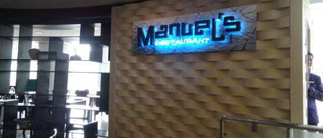 A restaurant interior with a neon sign reading "Manuel's Restaurant" on a textured wall.