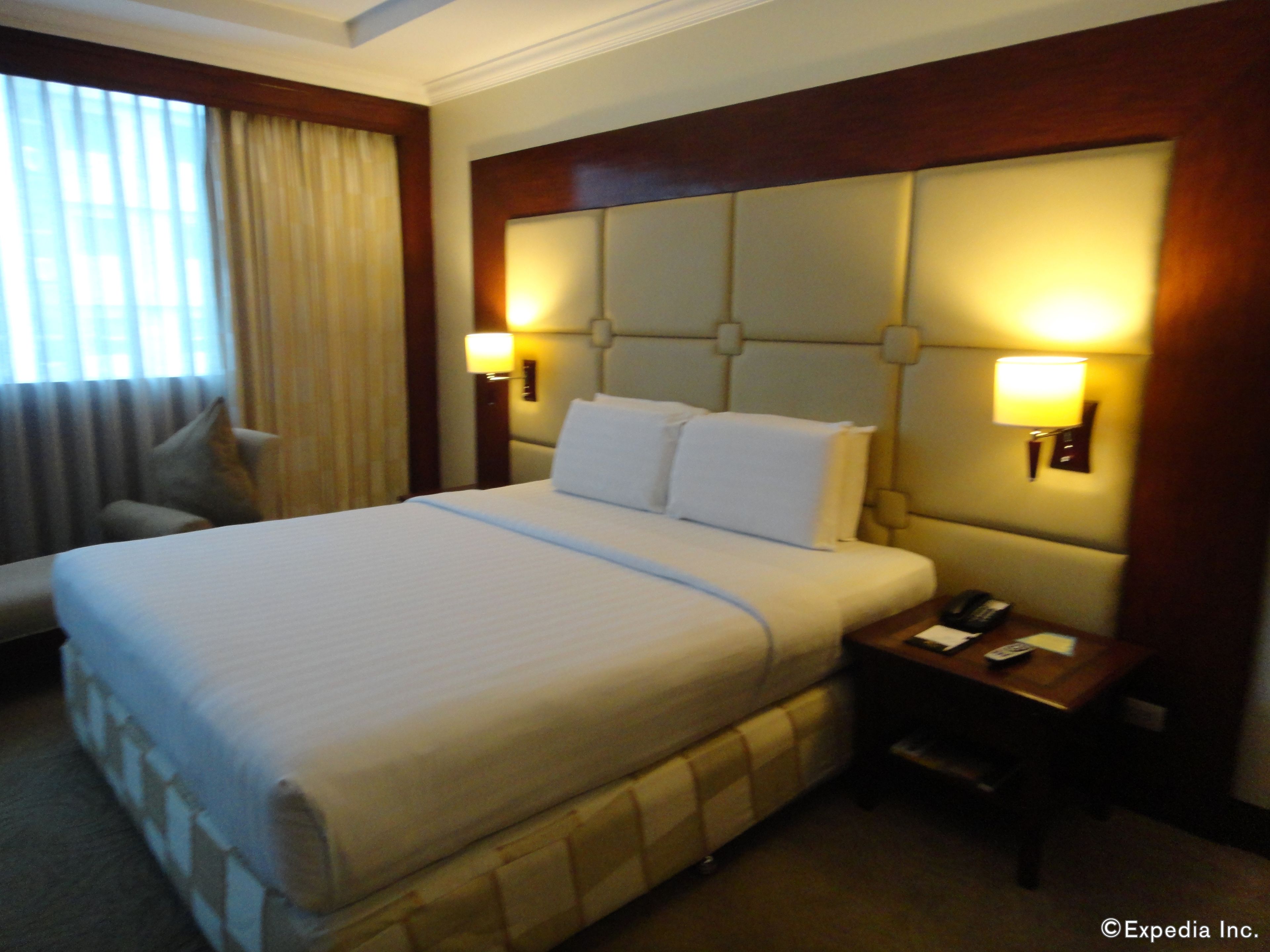 A hotel room with a large bed, two bedside lamps, a nightstand, a chair, and a window with curtains.