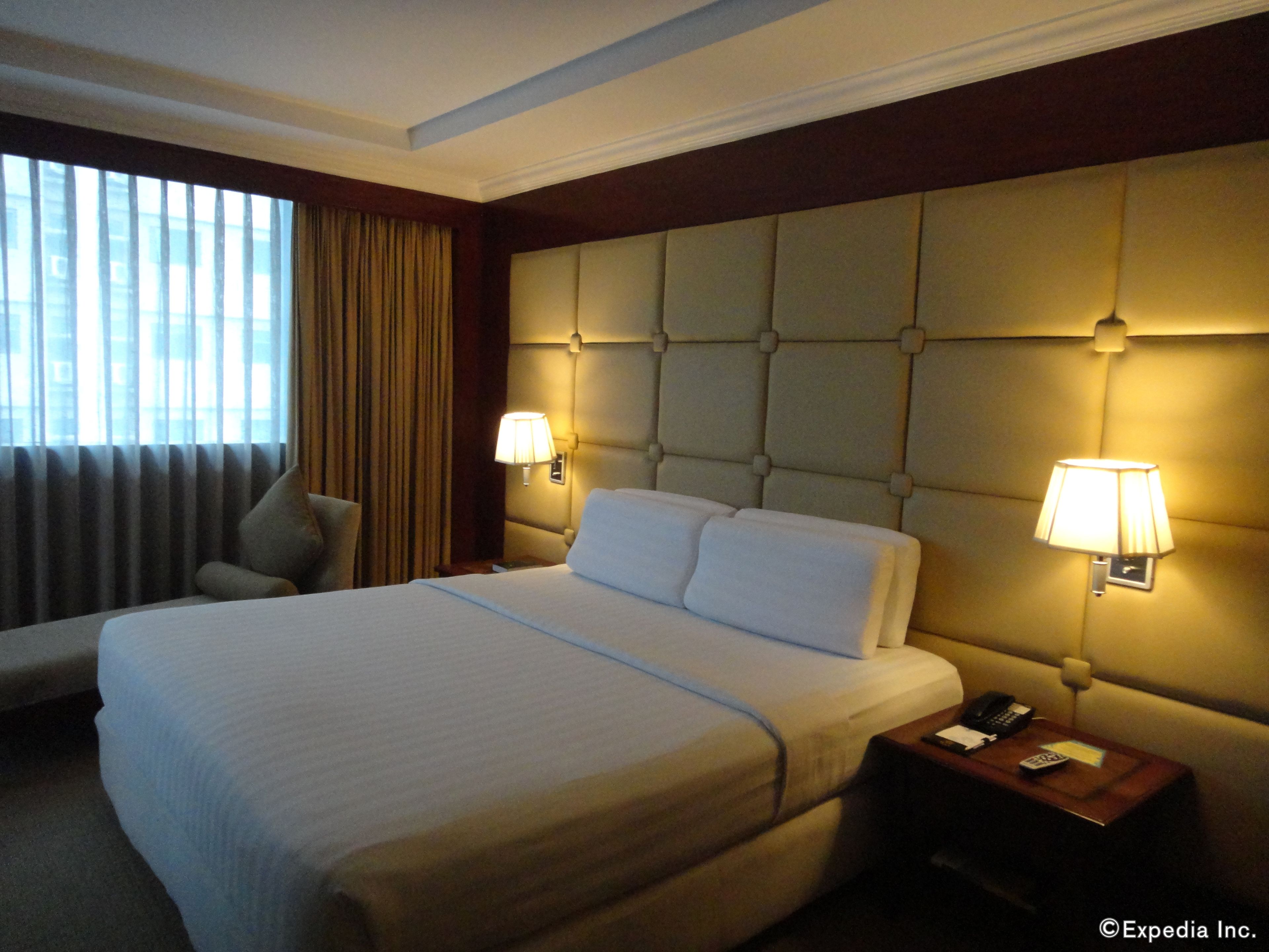 A hotel room with a large bed, two bedside lamps, a nightstand with a phone, and a chair.