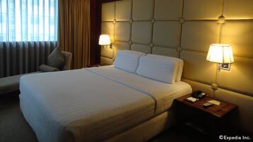 A hotel room with a large bed, two bedside lamps, a nightstand with a phone, and a chair.