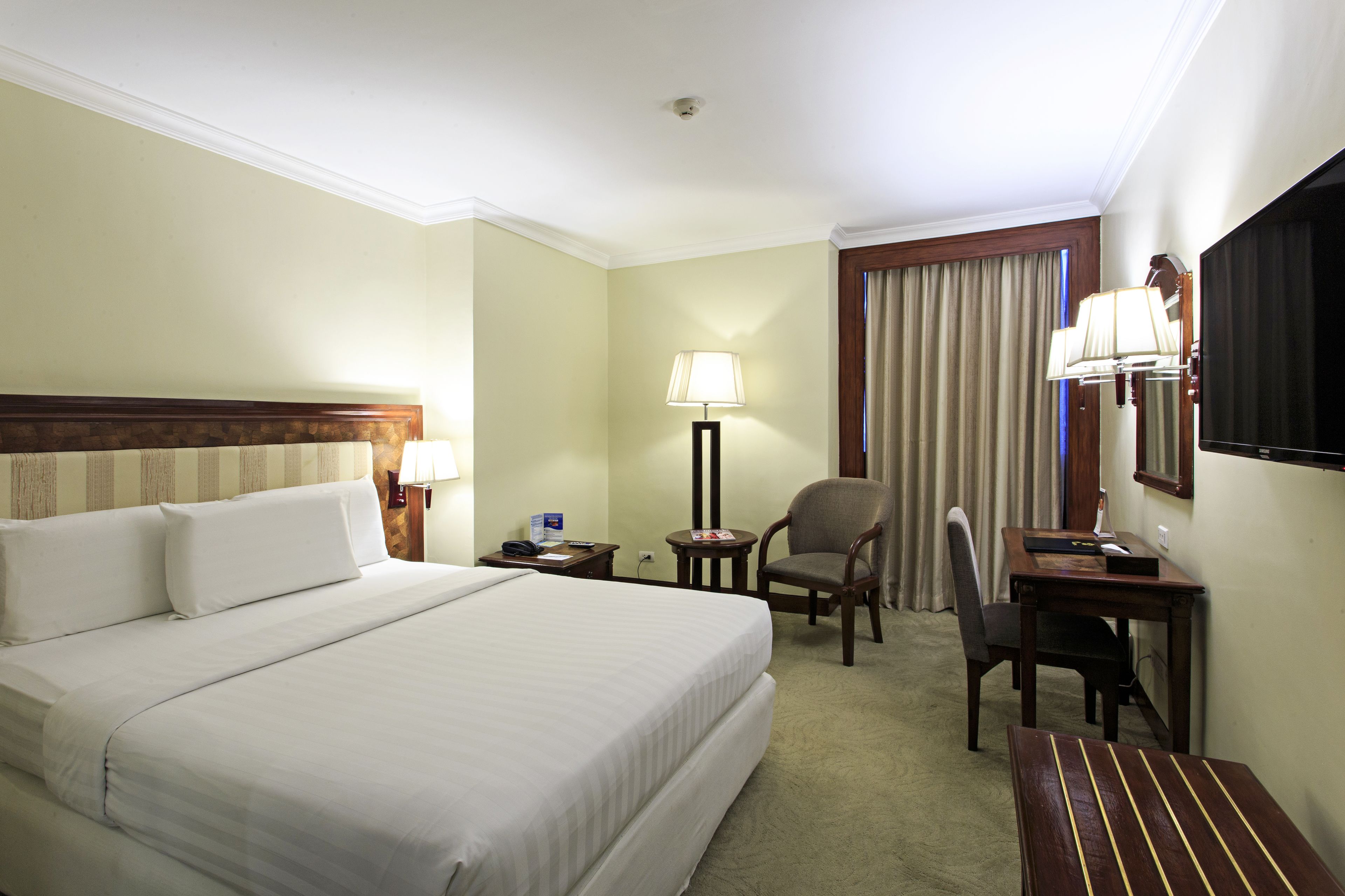 A hotel room with a large bed, two chairs, a desk, a lamp, and a window with curtains.